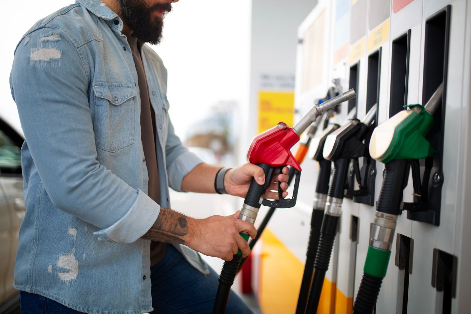Um homem de jaqueta jeans está em posto de gasolina abastecendo conforme as orientações da ficha técnica de carros.