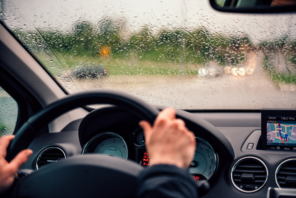 A imagem mostra a visão de dentro do carro de um motorista enquanto dirige na chuva.