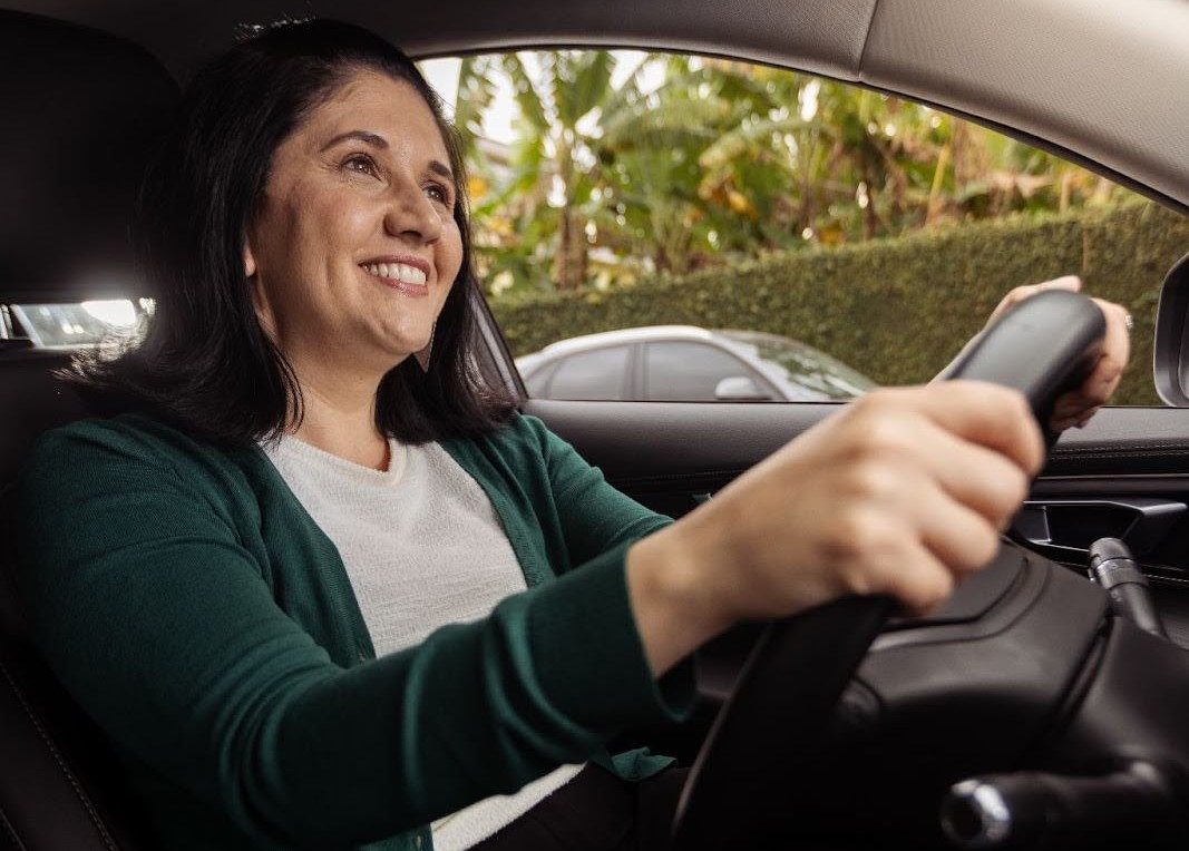 A imagem mostra uma motorista de blusa verde sorrindo ao saber o que é amperagem.