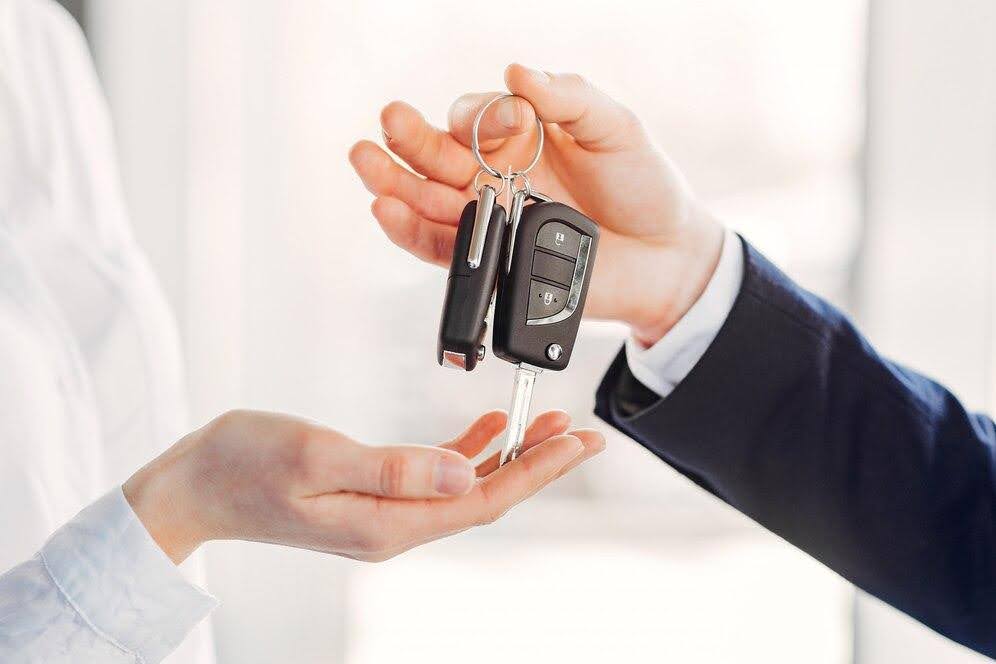 A imagem mostra uma pessoa entregando a chave de um carro para outra.