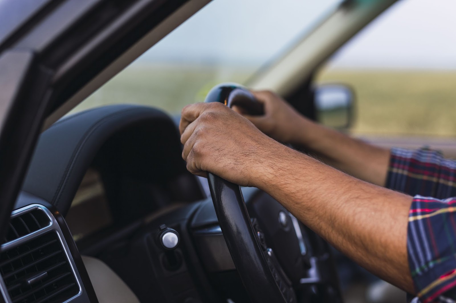 Imagem em foco próximo das mãos de um condutor segurando o volante de um automóvel equipado com um sistema de suspensão, capturada durante o dia.