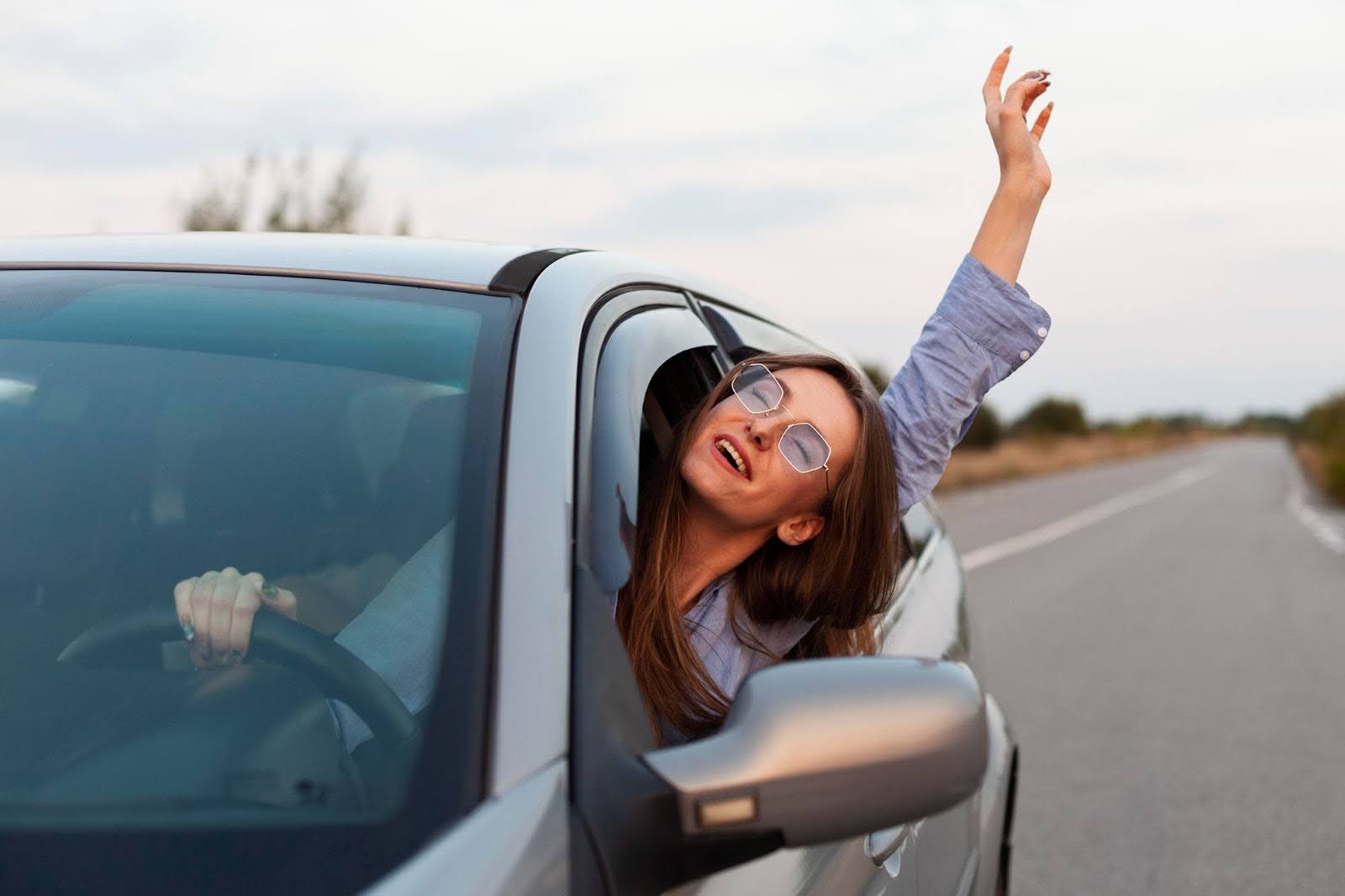 Na imagem, uma mulher de óculos escuros dirige pela estrada em um veículo cinza, contente com os benefícios do sistema de arrefecimento.