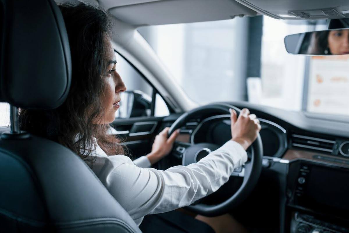 Imagem mostra uma mulher dirigindo um carro, olhando para o retrovisor e considerando a renovação da CNH.