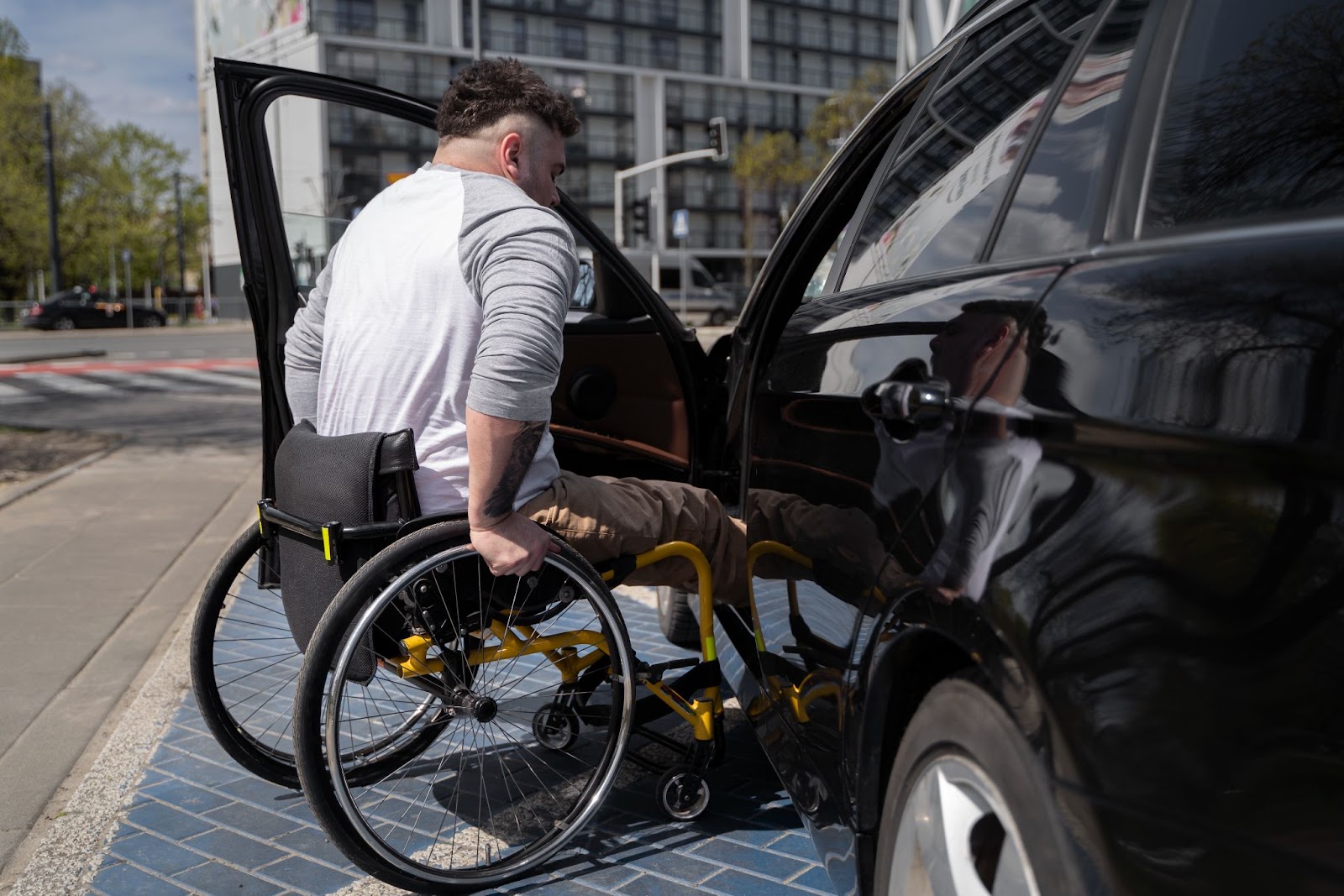 Na imagem, há um homem em uma cadeira de rodas entrando em um carro modificado, que possui o certificado de segurança veicular, estacionado em vaga preferencial.