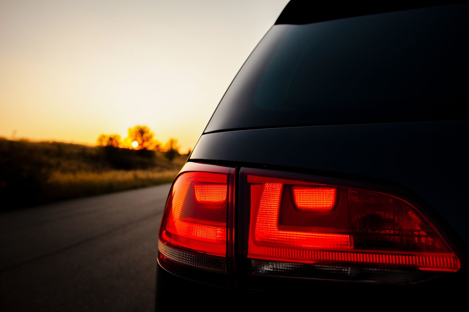 Close-up da lanterna traseira de um carro com o pisca alerta ligado enquanto o veículo está estacionado em um acostamento ao entardecer.