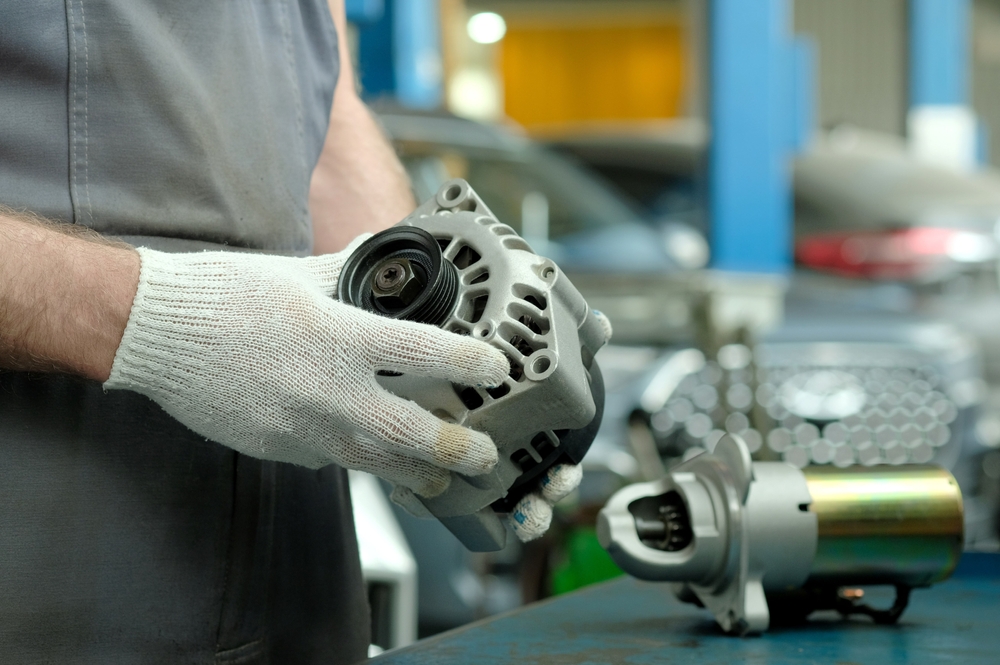 Close-up de um mecânico segurando um alternador de carro com uma luva.