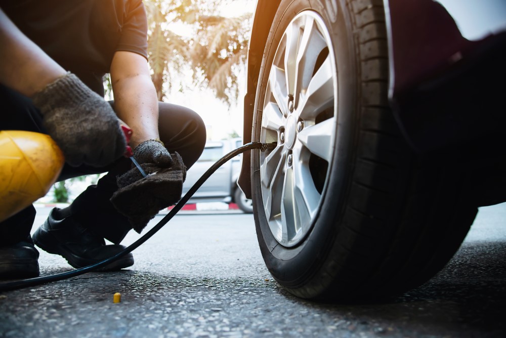 Homem agachado e com luvas calibrando pneu de um carro.