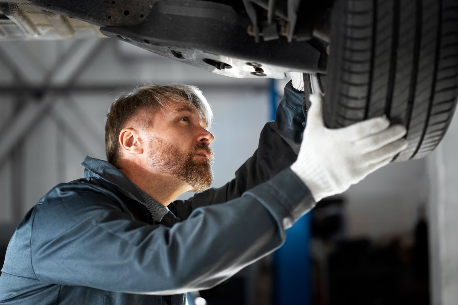 Homem mecânico examinando atentamente um dos componentes do sistema de suspensão de um veículo, o pneu.