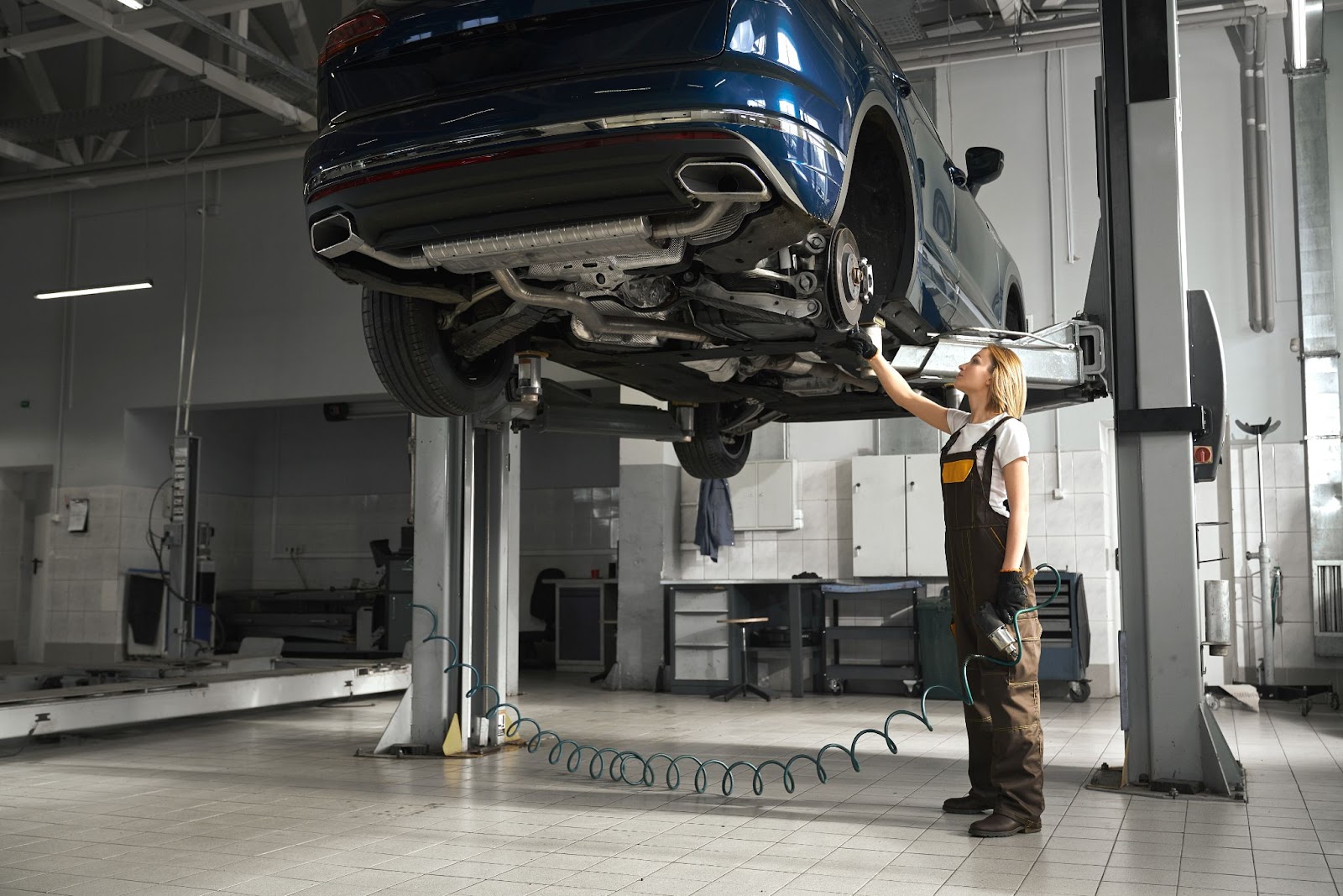 Uma mulher funcionária em uma oficina está examinando o sistema de suspensão de um automóvel de cor azul.