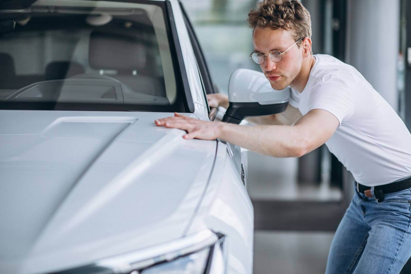 Foto mostra um homem branco loiro de óculos ao lado de um carro esportivo branco.