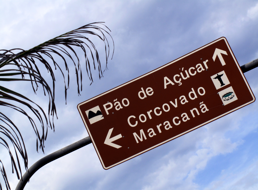 Foto mostra uma placa de sinalização turística marrom indicando a localização do Pão de Açúcar, Corcovado e Maracanã.