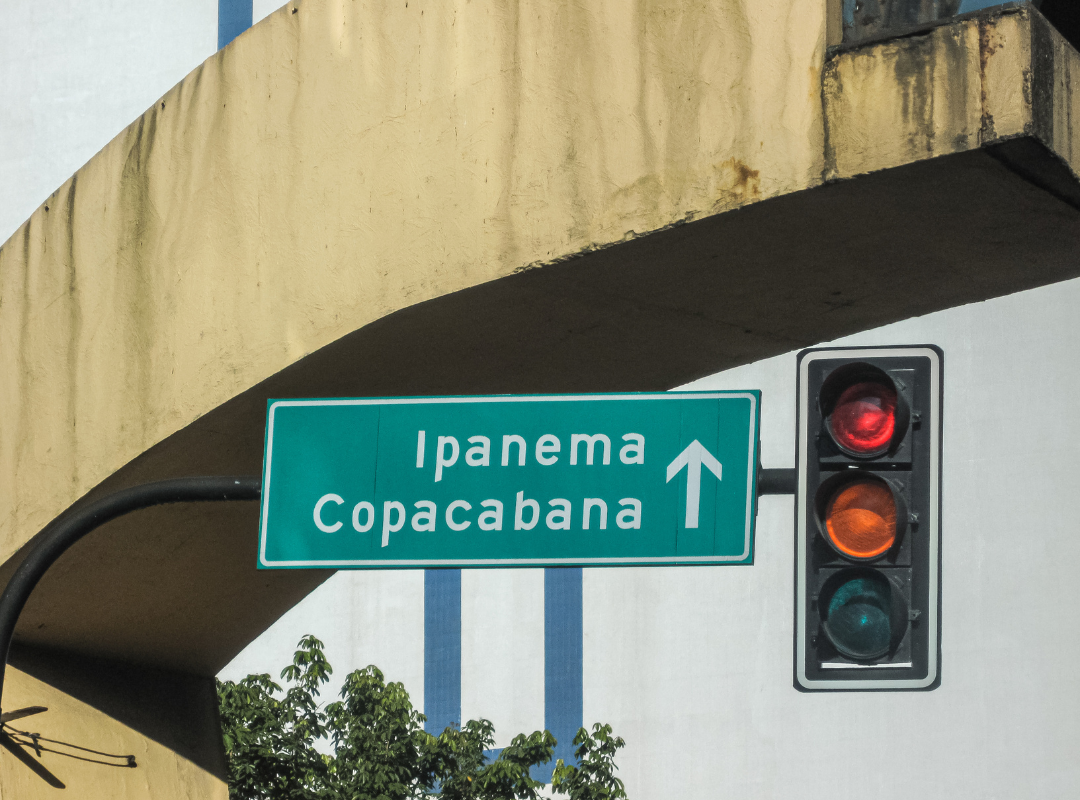 Foto mostra uma placa de sinalização verde ao lado de um semáforo indicando a direção de Ipanema Copacabana.