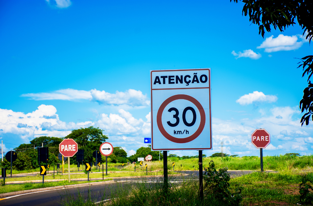 Foto mostra uma via com diversas placas de sinalização.