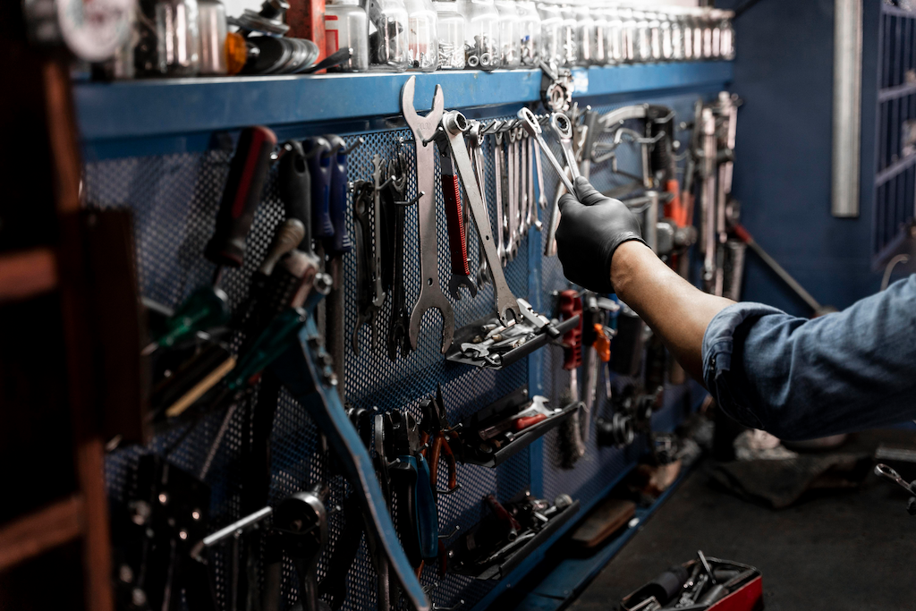 A imagem mostra um painel com várias ferramentas e a mão de um mecânico pegando uma delas.