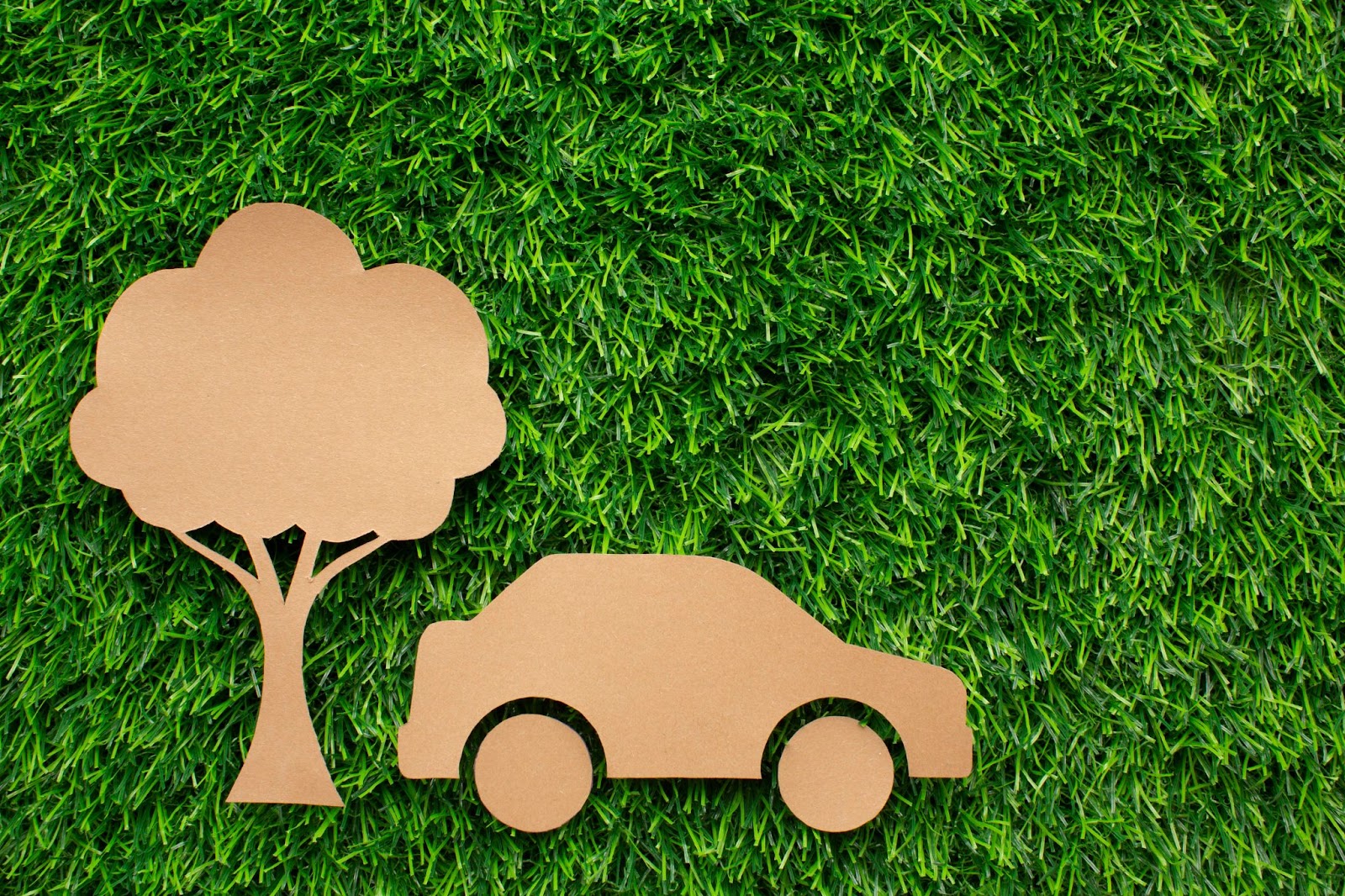 Imagem de um carro e uma árvore recortados em material de papelão em cima da grama representando a mobilidade urbana sustentável.