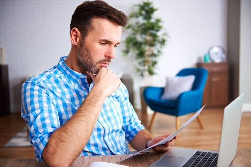 Imagem de um homem de camisa xadrez azul pesquisando em um notebook a diferença entre suspensão e cassação.