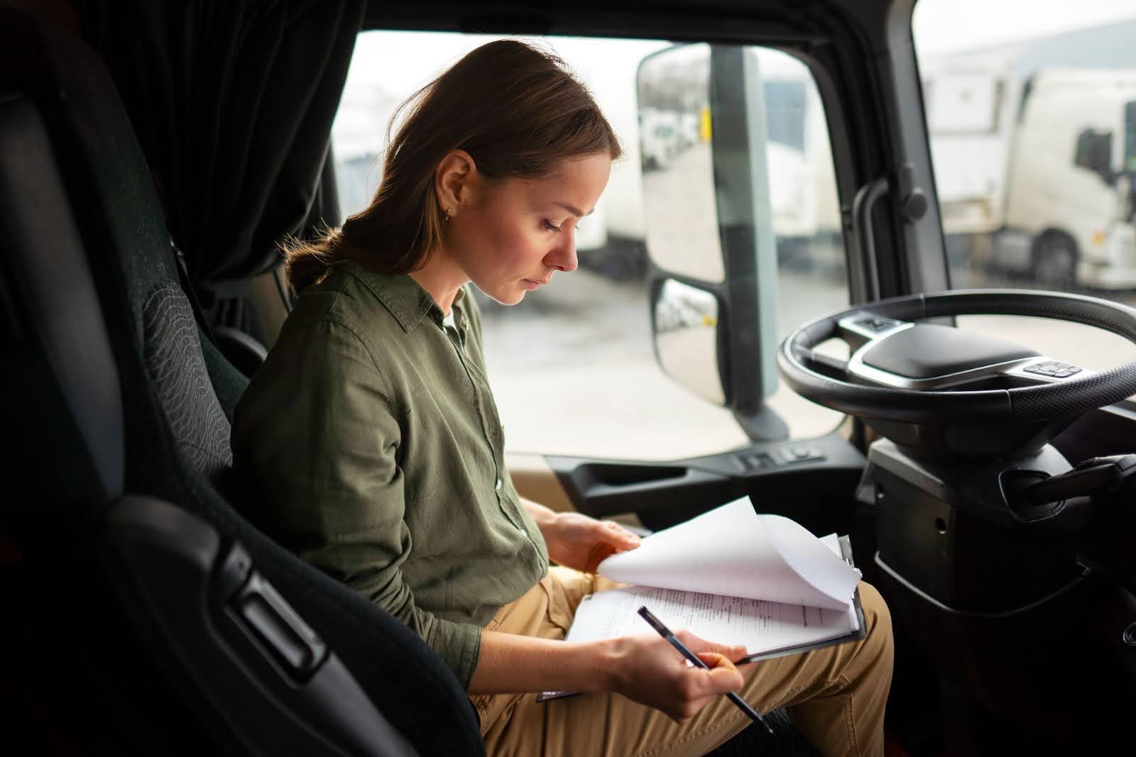 imagem de uma motorista de camisa verde ao volante de um caminhão verificando documentação sobre CNH categoria D.