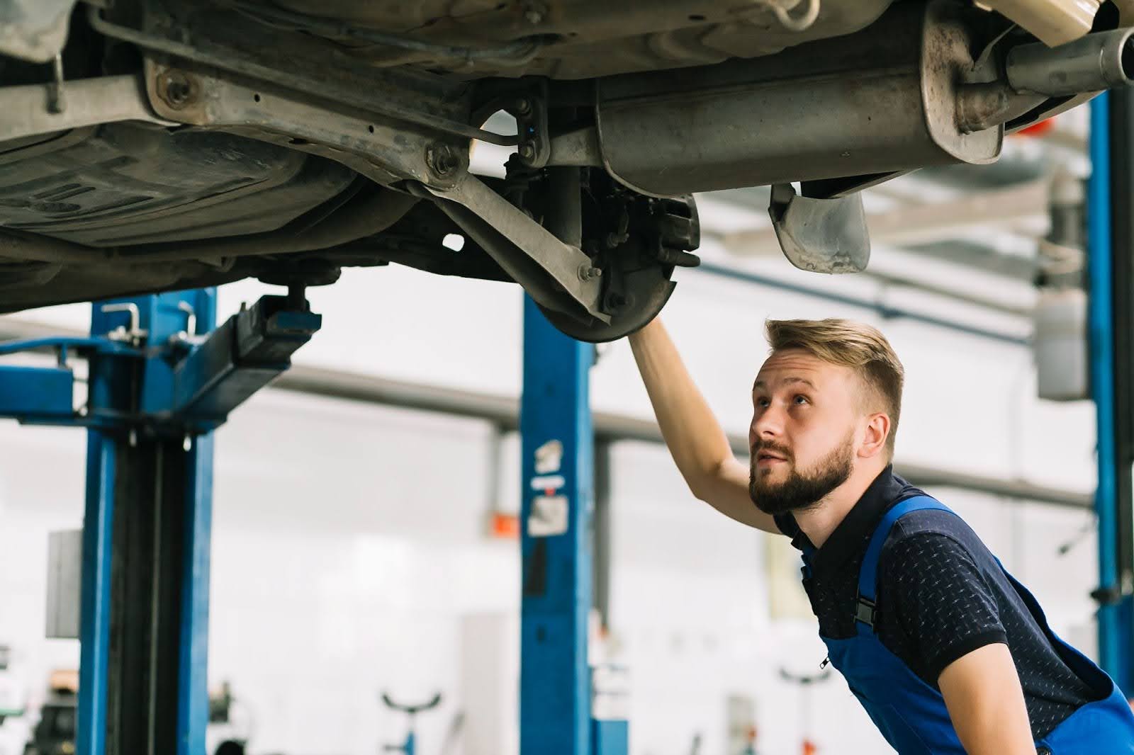 Imagem mostra um mecânico observando a parte inferior de um automóvel suspenso, mostrando seu escapamento apresentando o que é catalisador.