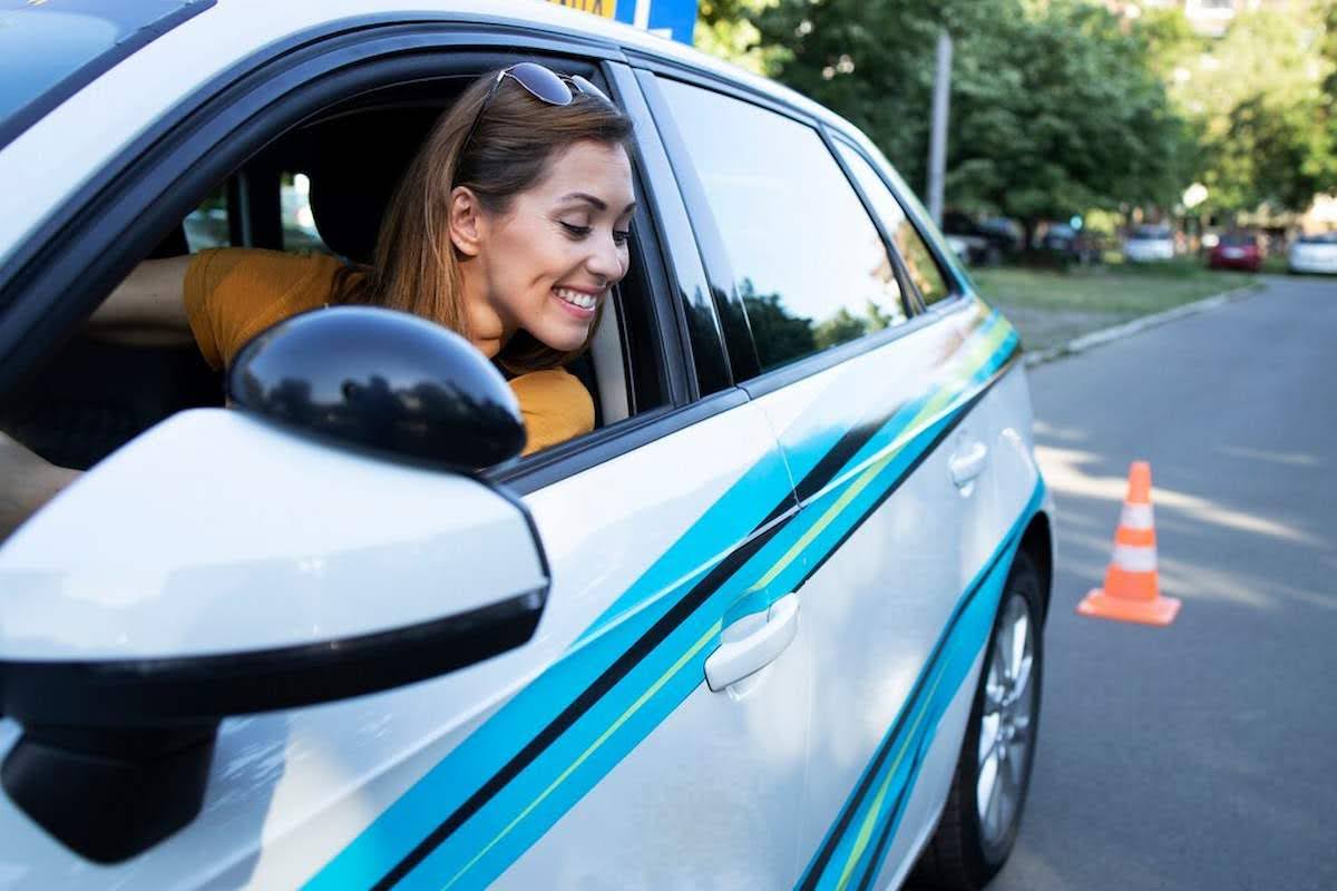 Imagem mostra uma mulher dirigindo um carro, dando ré em direção a um cone. Indicando a baliza na prova de direção.