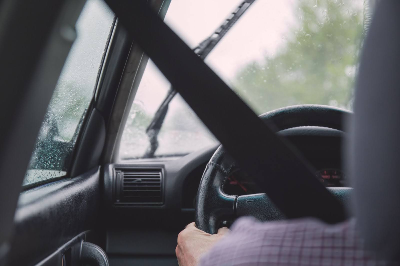 Cinto de segurança protegendo um motorista, que dirige seu carro num dia chuvoso.