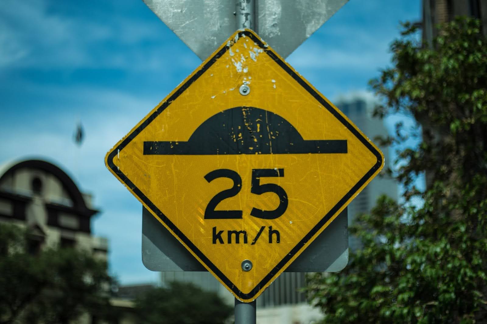 Placa losangular amarela sinalizando 25 km/h como o limite de velocidade permitida.