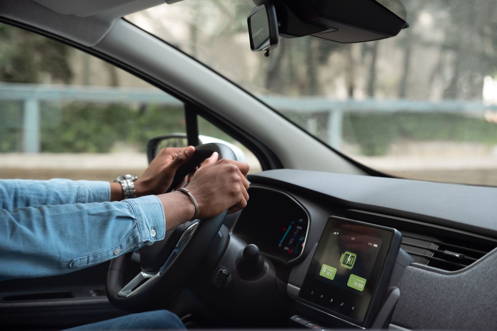 Imagem retratando as mãos de um indivíduo que sabe como funciona um carro elétrico segurando o volante, enquanto o painel exibe a quantidade de energia restante para recarga.