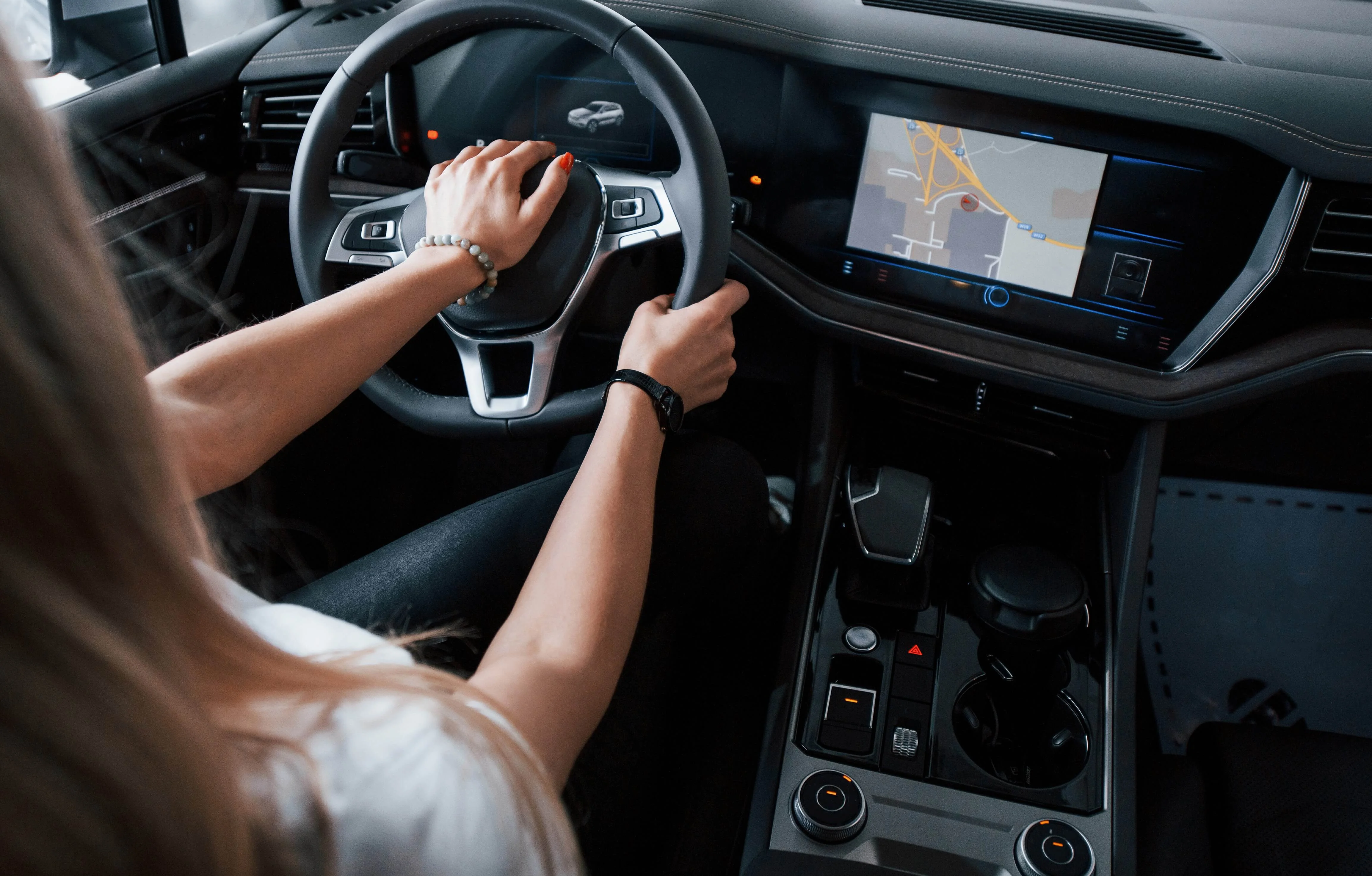 Visão interna de um automóvel, na qual uma mulher de camisa branca está com as duas mãos no volante