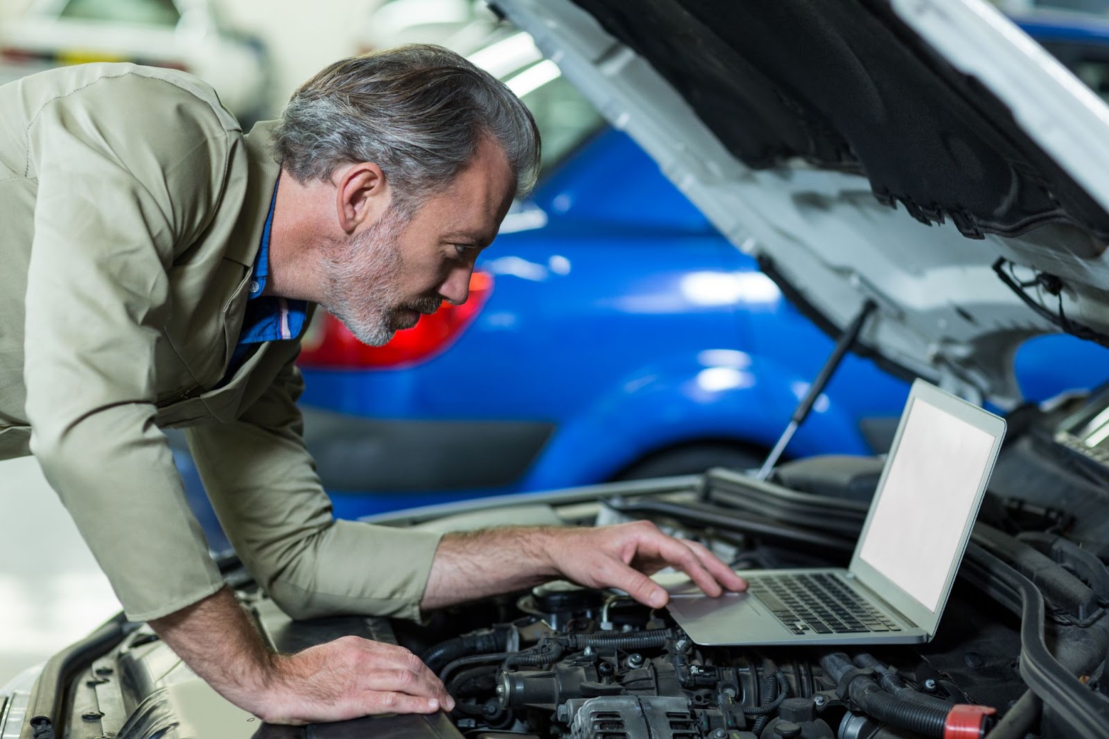 Mecânico atento utilizando um notebook que está apoiado em cima do sistema de injeção eletrônica de um carro.