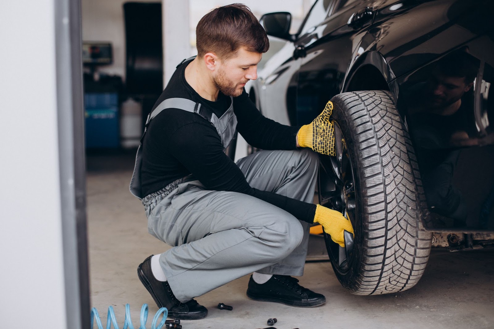 Mecânico fazendo a troca do pneu desgastado de um veículo em uma oficina. Ele veste macacão cinza e luvas amarelas.