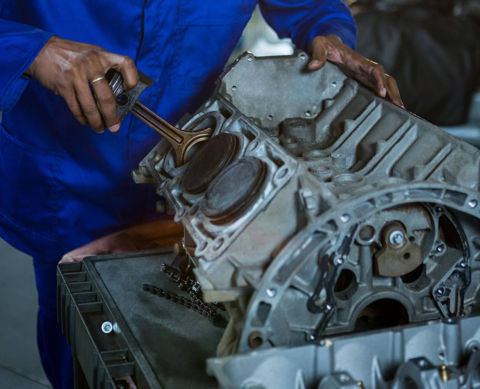 Na imagem um homem de azul encaixa um cilindro em um motor em V do tipo V6.