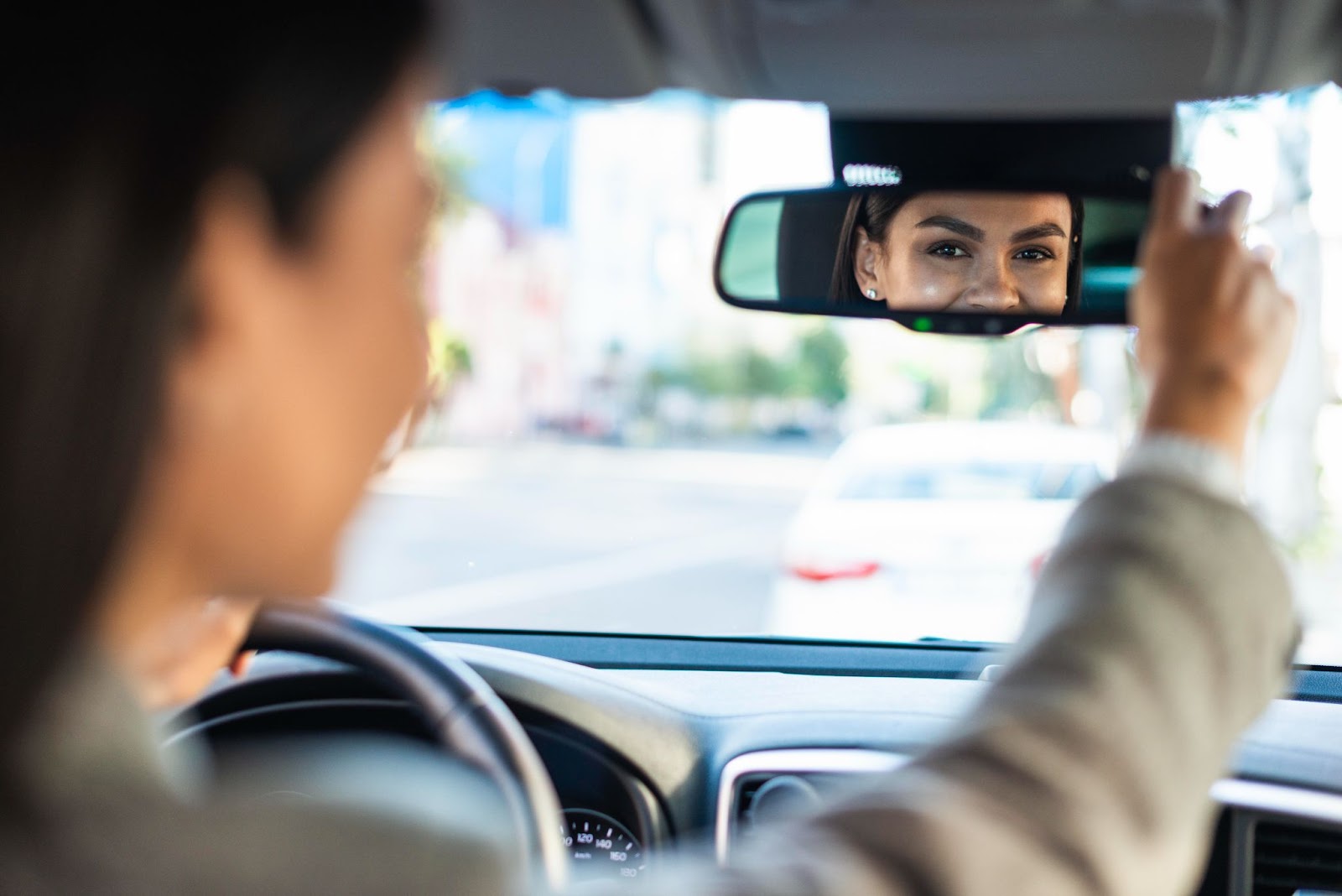 Mulher ajustando o retrovisor do seu carro antes de dirigir, um dos principais itens de segurança do veículo.