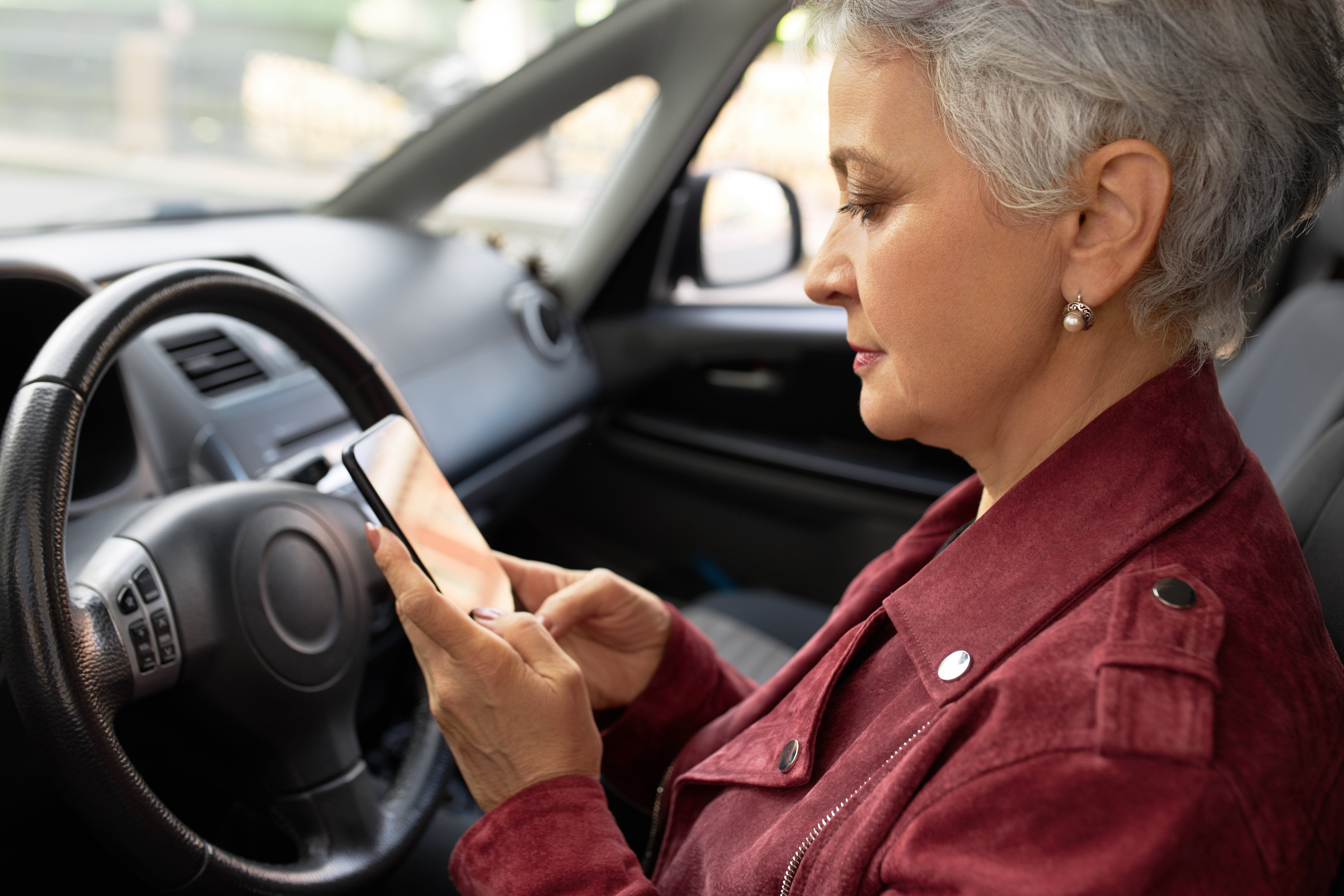 Mulher idosa dentro de um carro, usando o celular para consultar o bloqueio RENAJUD