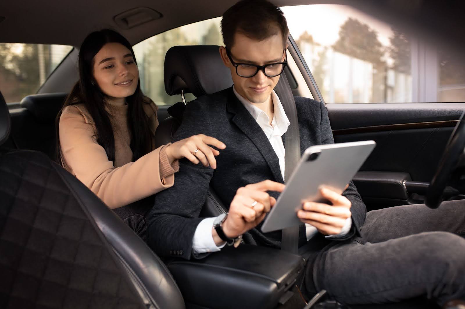 mulher no banco de trás de um carro parado apontando para um tablet nas mãos do motorista