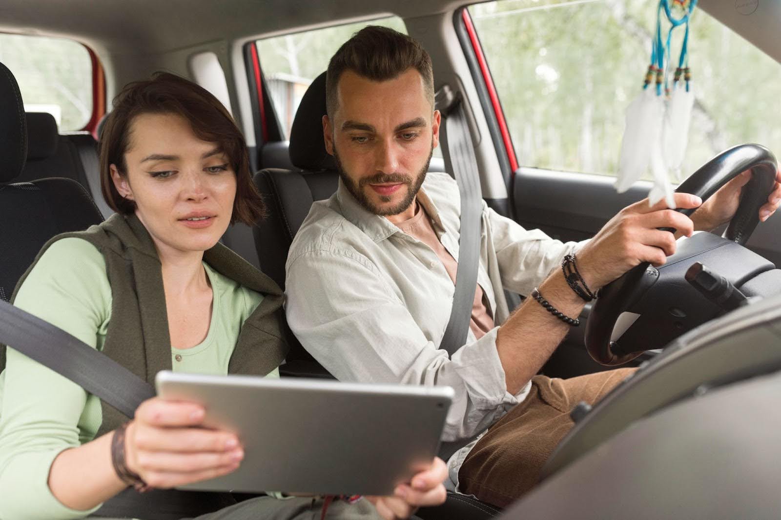 mulher no banco do carona de um carro mostrando um tablet ao motorista onde pesquisou onde fica o código de segurança da CNH.