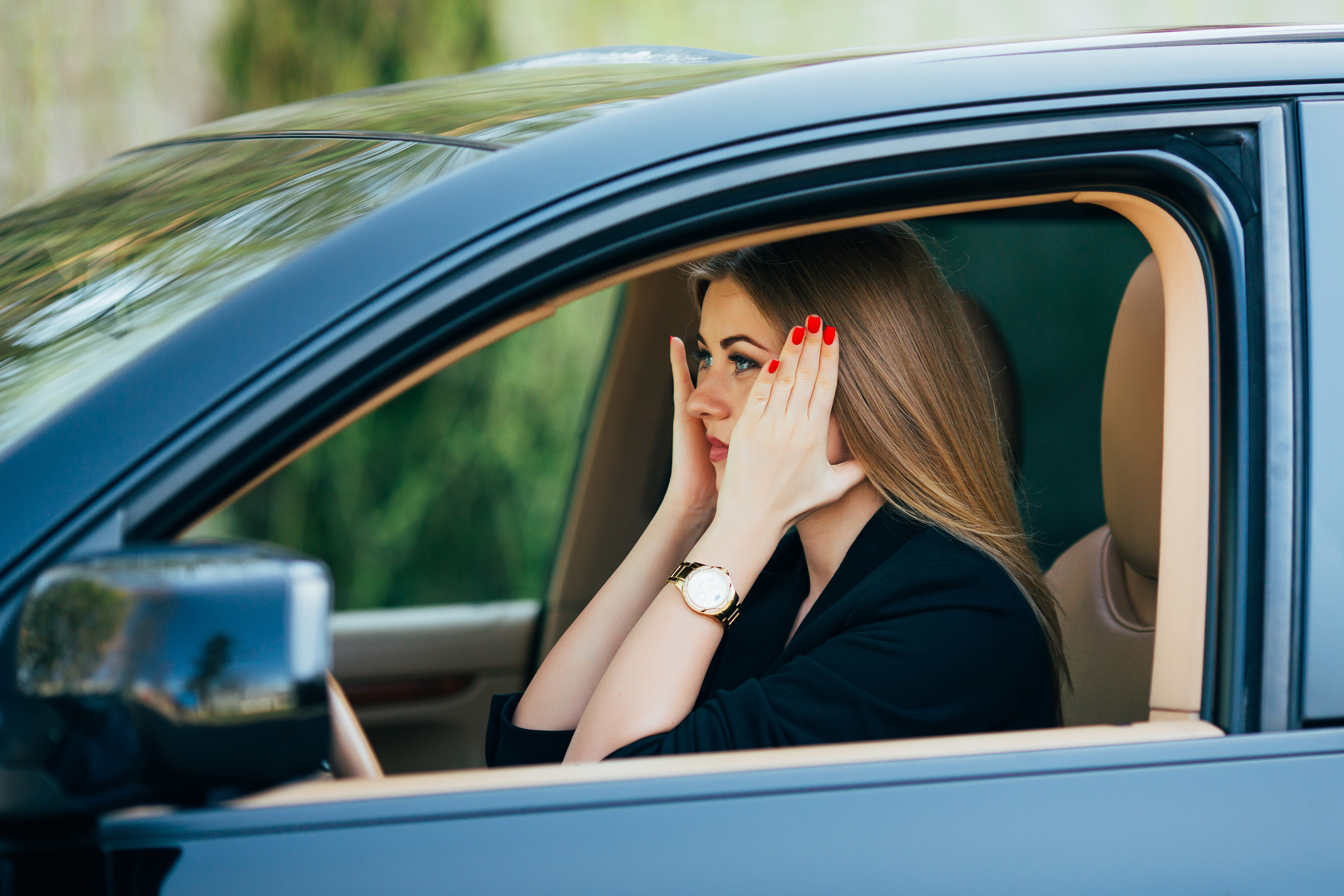 Mulher preocupada no volante após descobrir que a CNH está suspensa. Ela apoia as duas mãos no rosto e está com expressão séria.