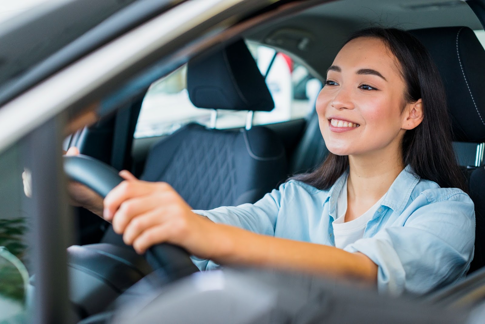 Mulher vestindo roupas social enquanto dirige um carro com bateria EFB com as duas mãos no volante e está com expressão feliz.