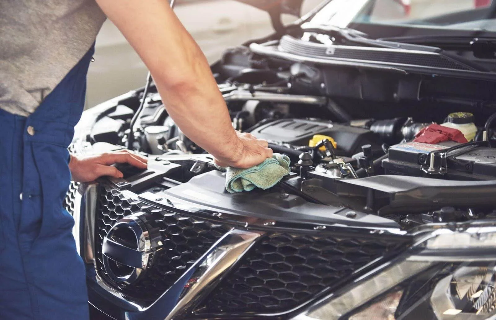 Na imagem, um mecânico está limpando o zinabre da bateria de um carro com um pano.