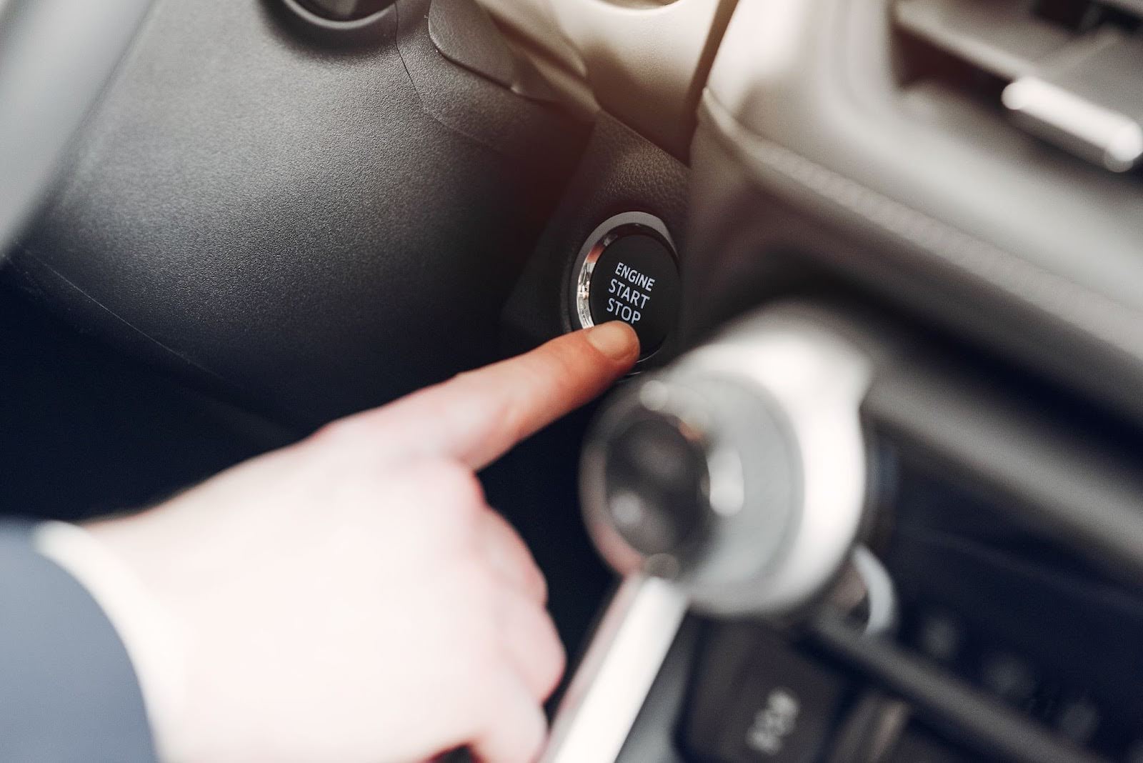 Close-up de uma mão pressionando o botão de partida do carro com o recurso start-stop, parte do sistema keyless.