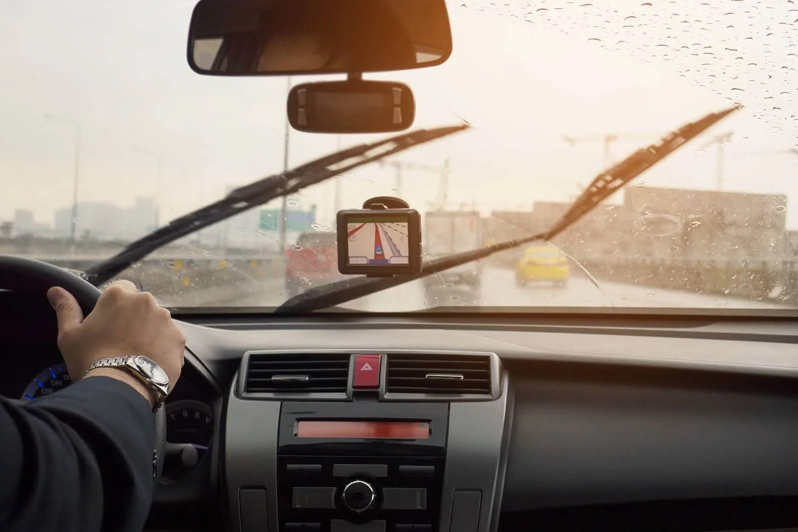 Na imagem há a visão interna de um motorista dirigindo o carro no trânsito olhando para o para-brisa com o vidro embaçado.