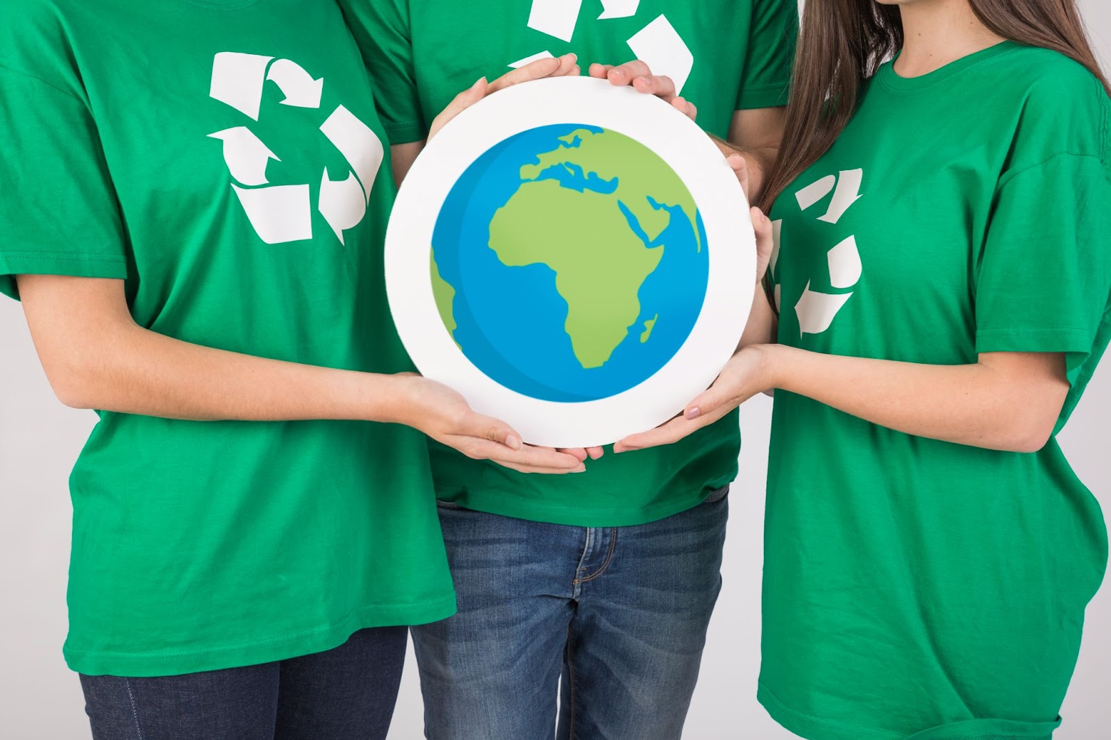 Um grupo de três pessoas está vestindo camisetas verdes, cada uma delas exibindo o símbolo da reciclagem, enquanto seguram uma imagem ilustrada do planeta Terra.