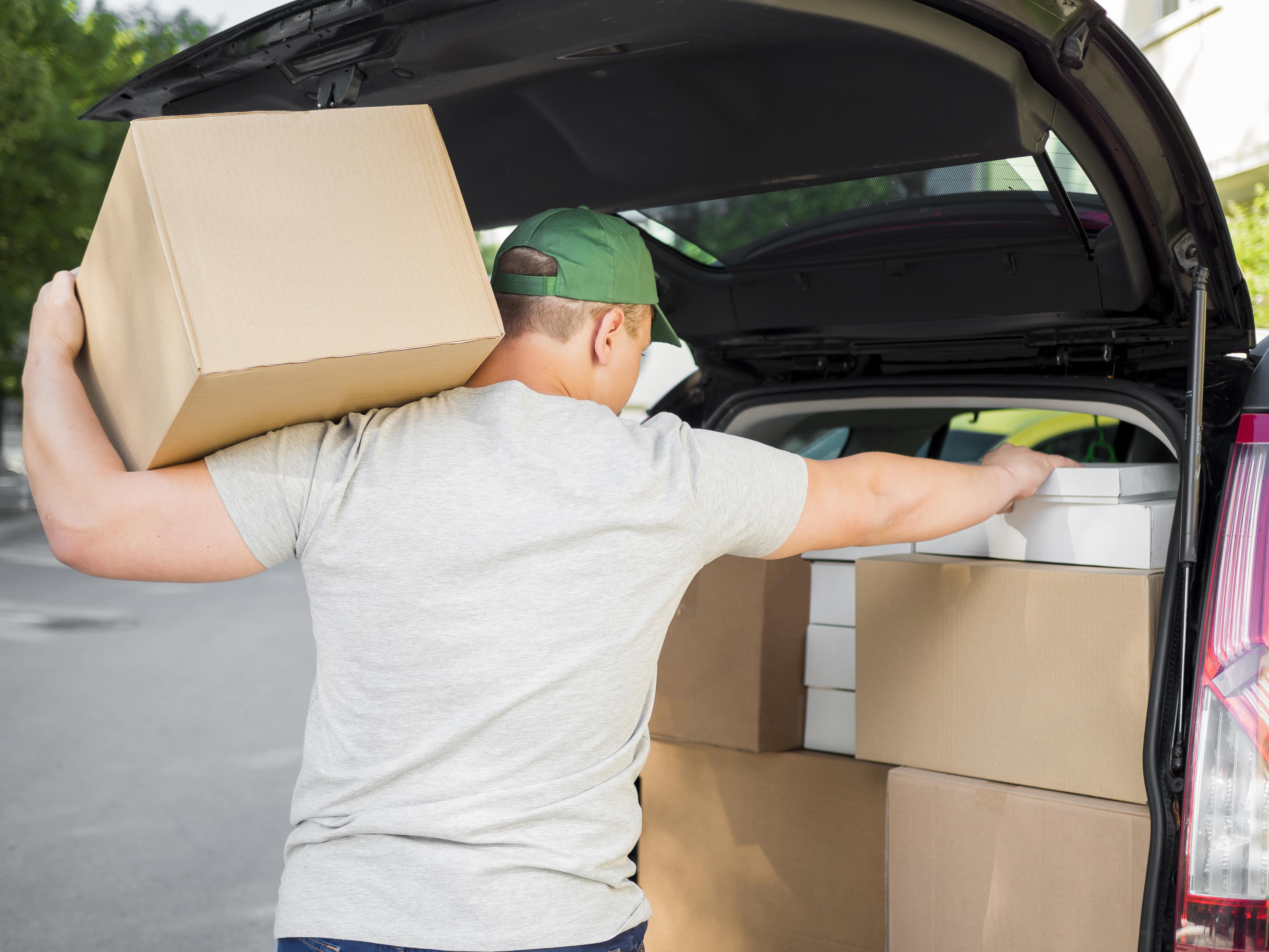 Um homem de camisa cinza e boné verde abastece um veículo com várias caixas pesadas.