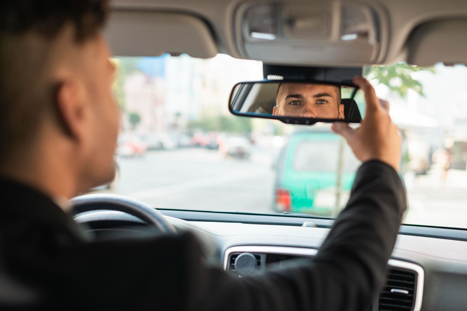 Um homem dentro do carro verificando o retrovisor para assegurar uma distância de seguimento adequada. No retrovisor, é possível ver o reflexo do rosto do motorista.