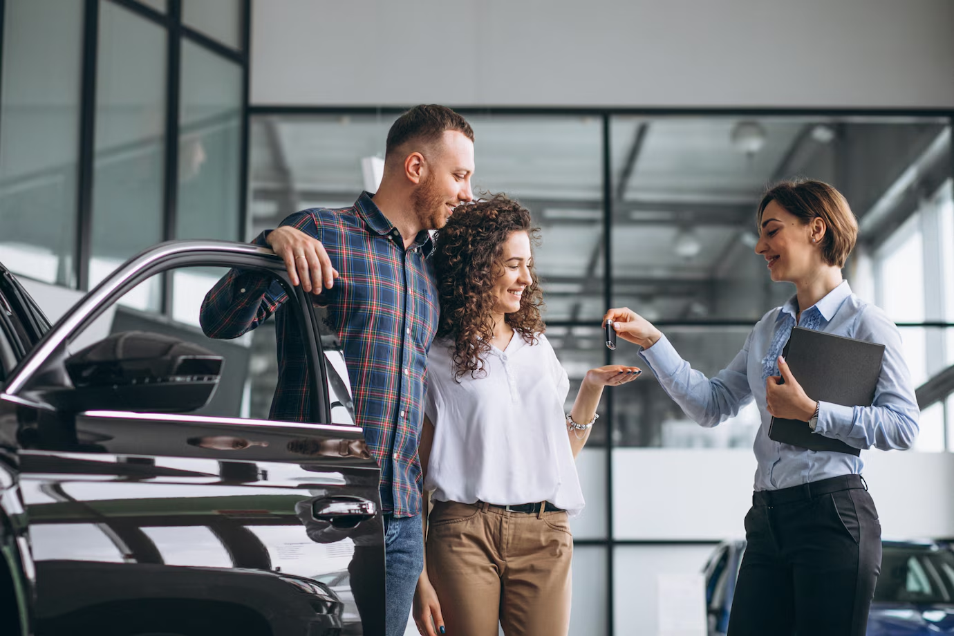 Um homem e uma mulher está recebendo as chaves de um carro novo de uma vendedora em uma concessionária. 