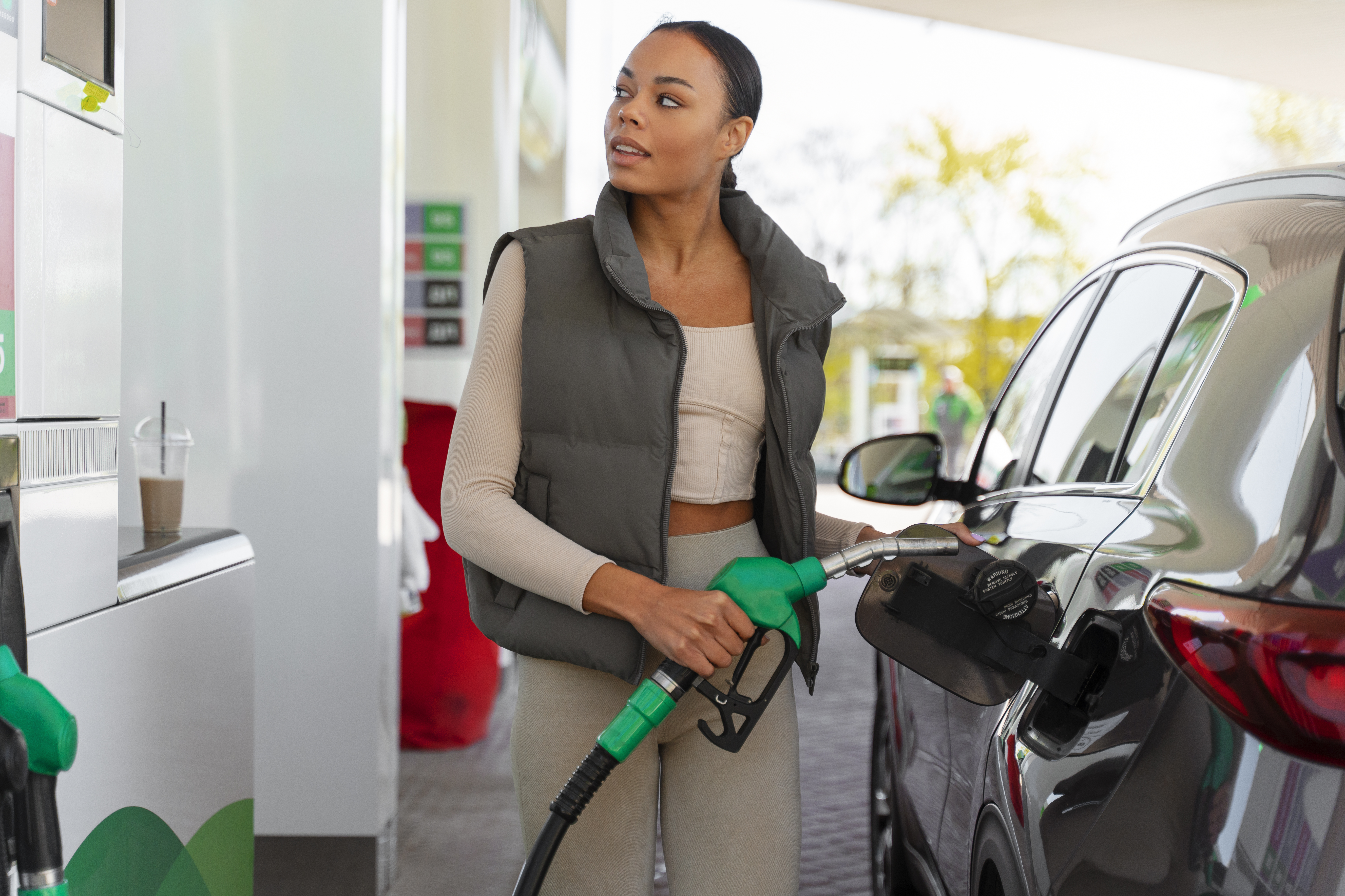 Uma mulher de colete cinza está abastecendo seu veículo atenta a sinais de desgaste no filtro de combustível. 