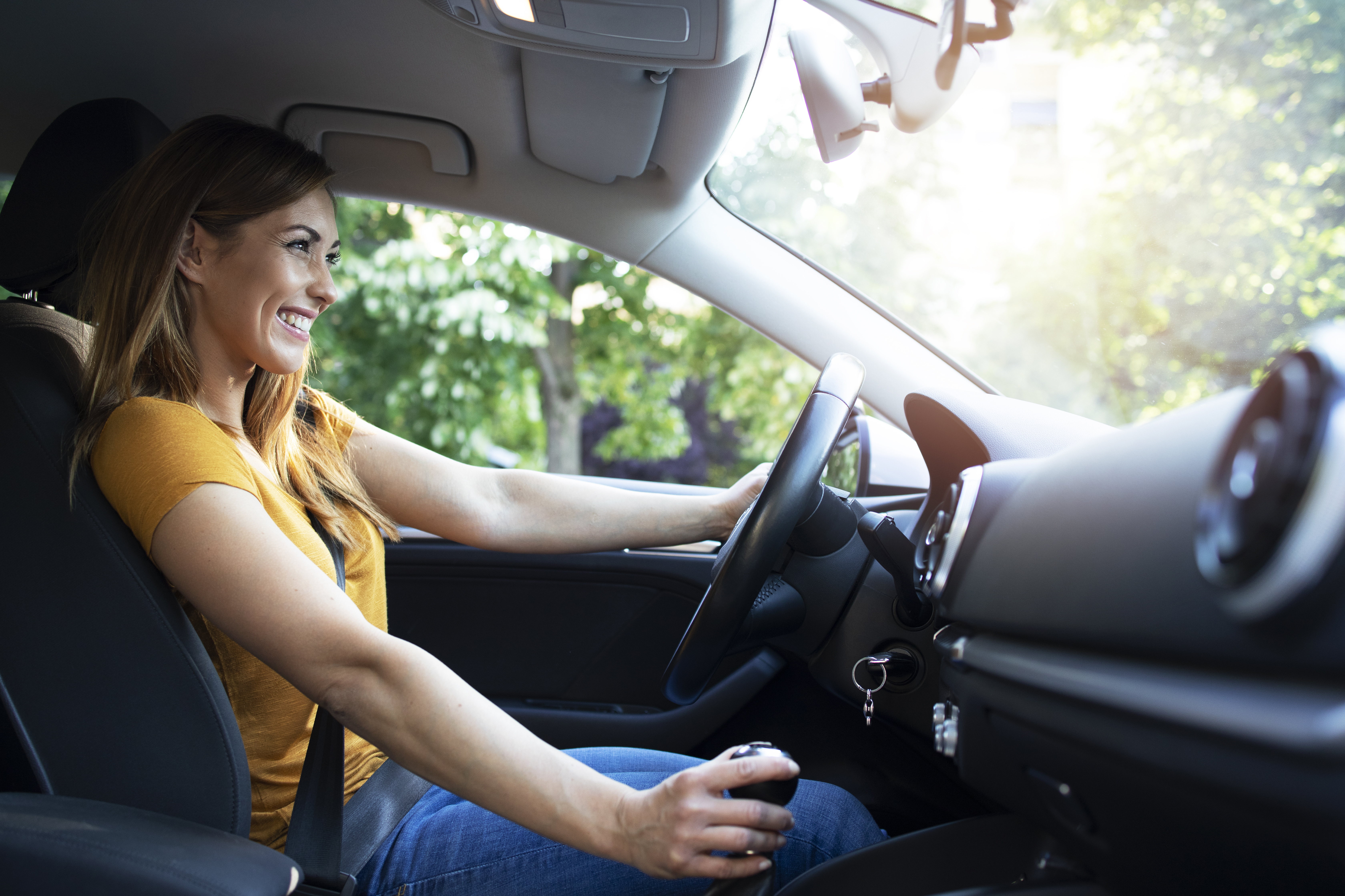 Uma mulher loira sorri enquanto dirige suavemente para não prejudicar a junta homocinética do veículo.