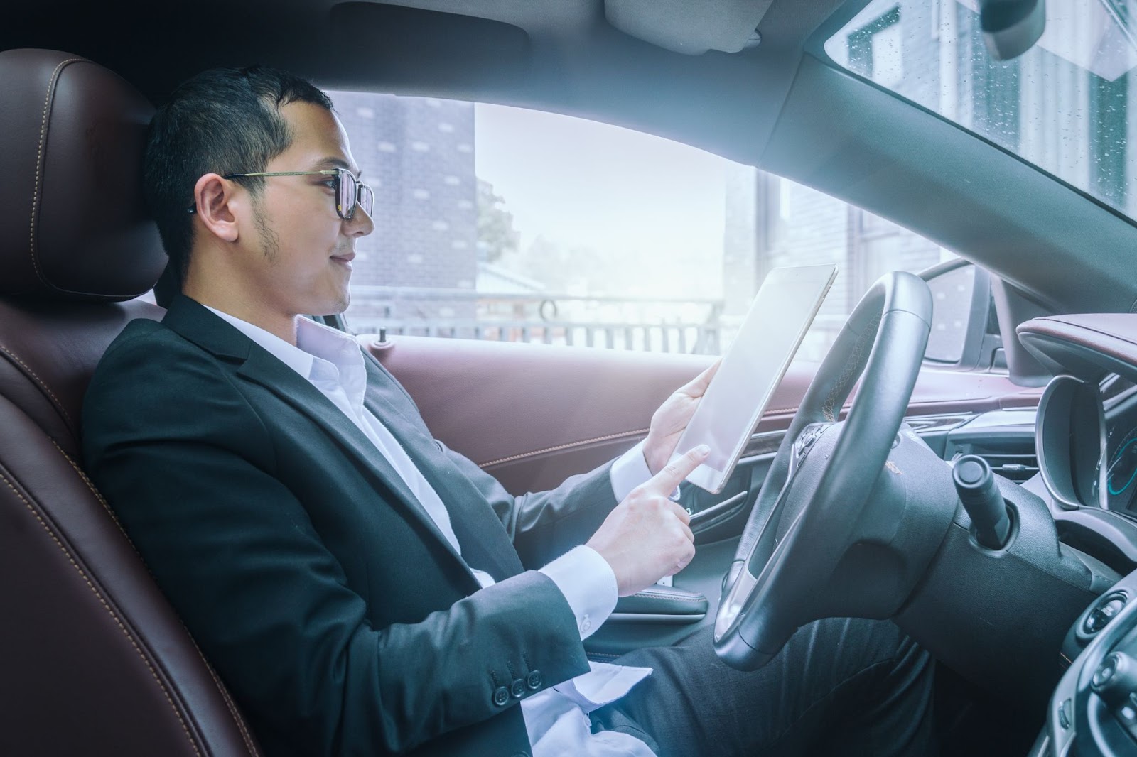 Homem vestindo roupa social dentro de um carro autônomo enquanto mexe em um tablet.