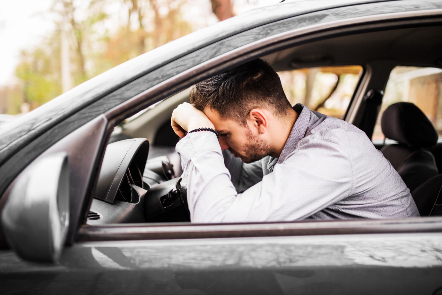Um homem debruçado sobre o volante de um carro, demonstrando preocupação.