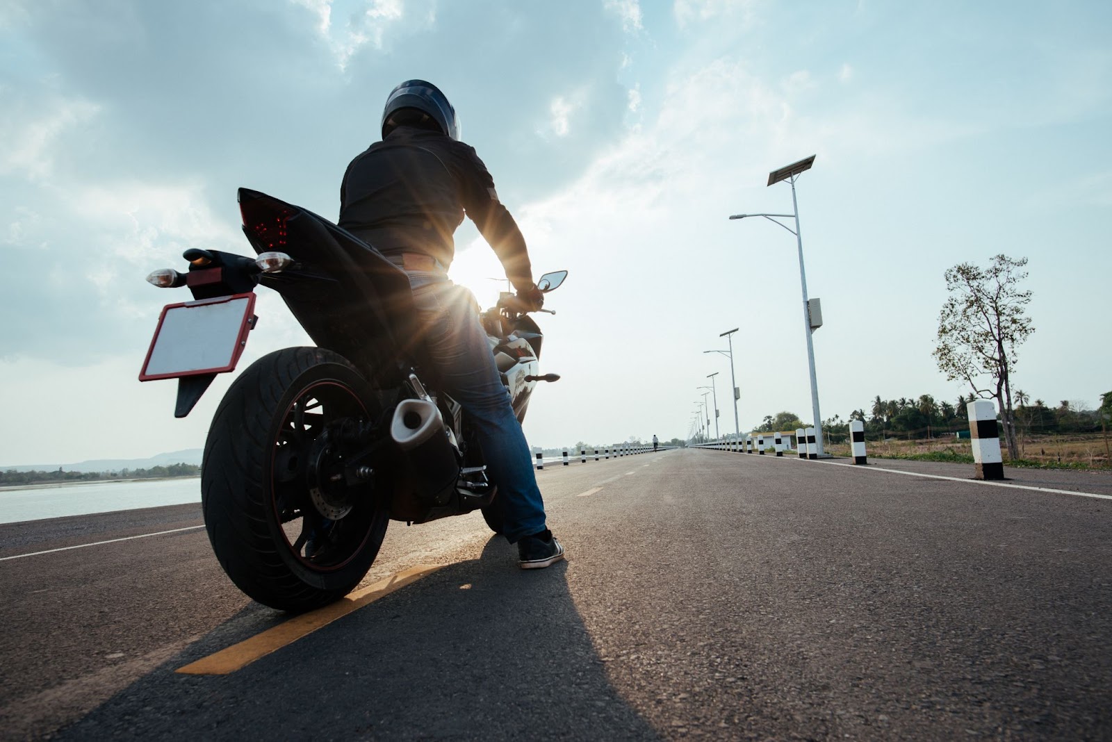 Imagem de vista de trás de motociclista em uma estrada se preparando para viajar de moto durante o dia.