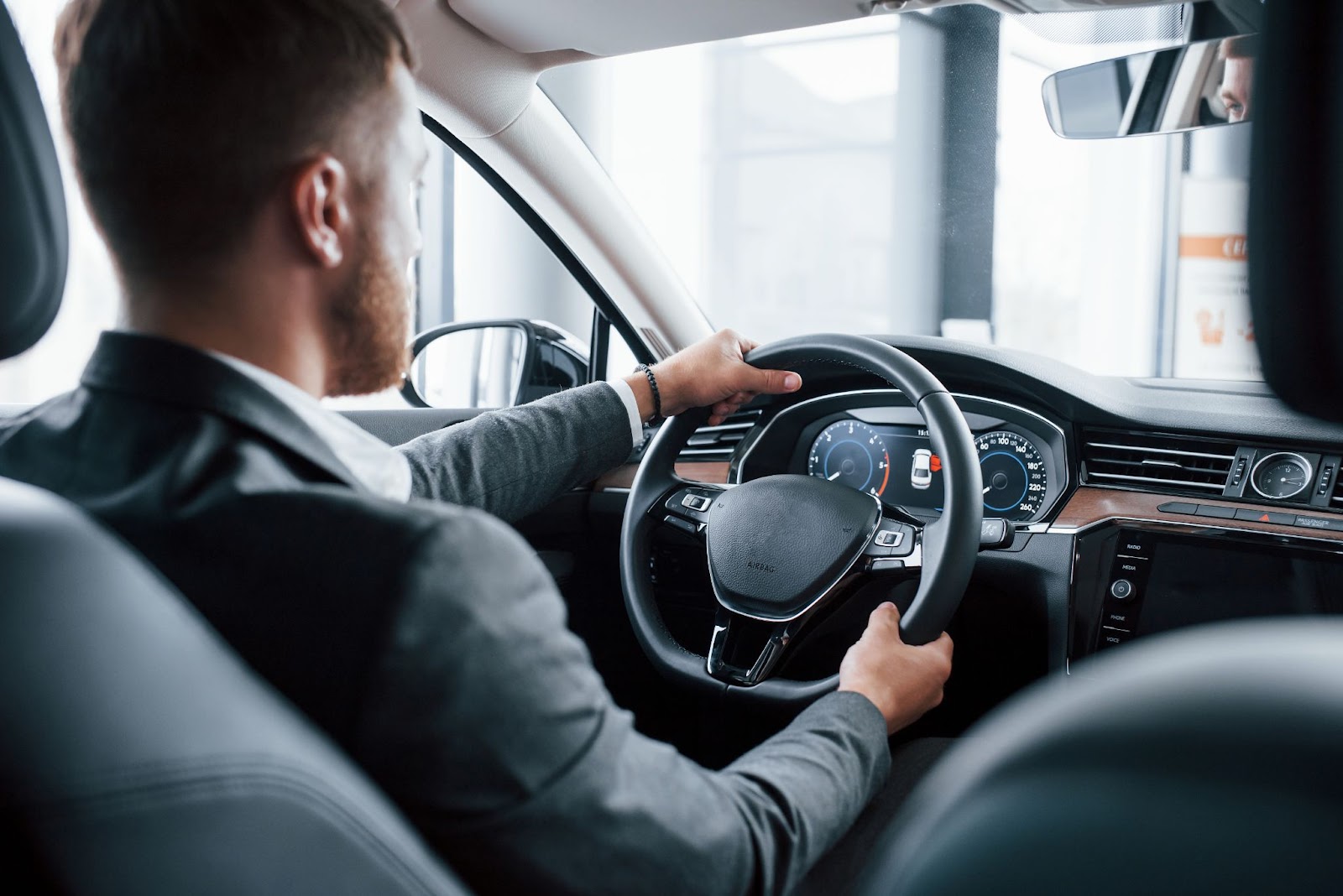 Imagem vista de trás de um motorista dentro de carro apoiando as mãos no volante e satisfeito com a direção assistida.