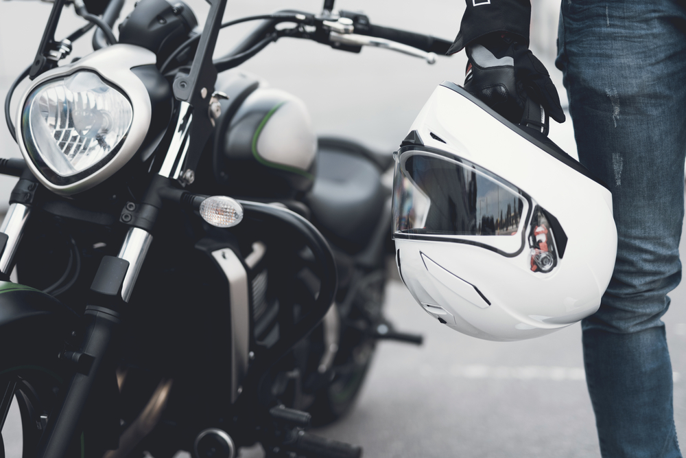 Close-up de motoqueiro ao lado de sua motocicleta vestindo calça jeans e segurando um capacete.